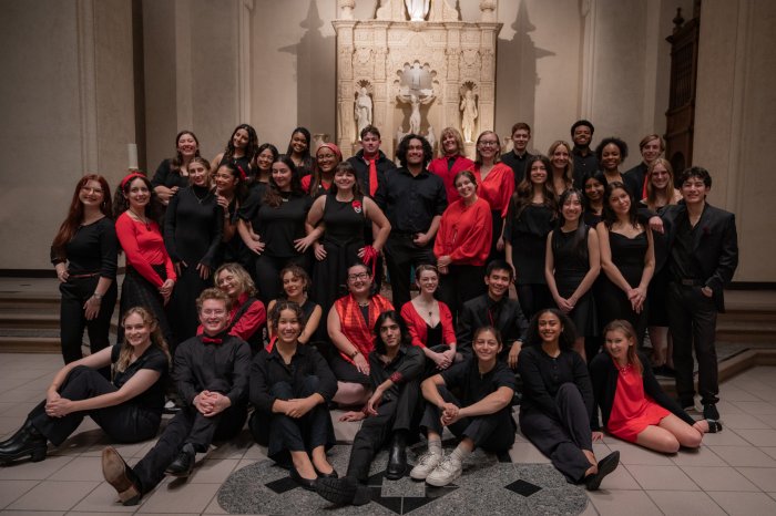 SMC Choir Fall '25 with students standing and sitting in front of the altar dressed in black with red accents.