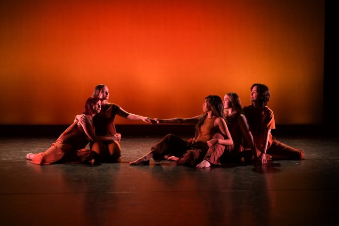 Dancers sitting on stage posed with an dark orange background