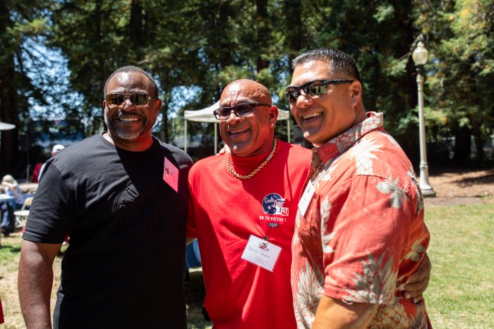 Three former football players embrace at a tailgate