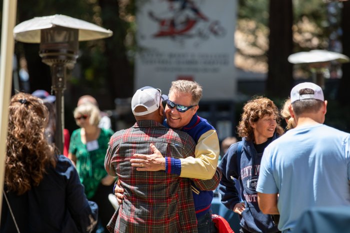 Two alumni embrace in the Redwood Grove during a barbecue picnic