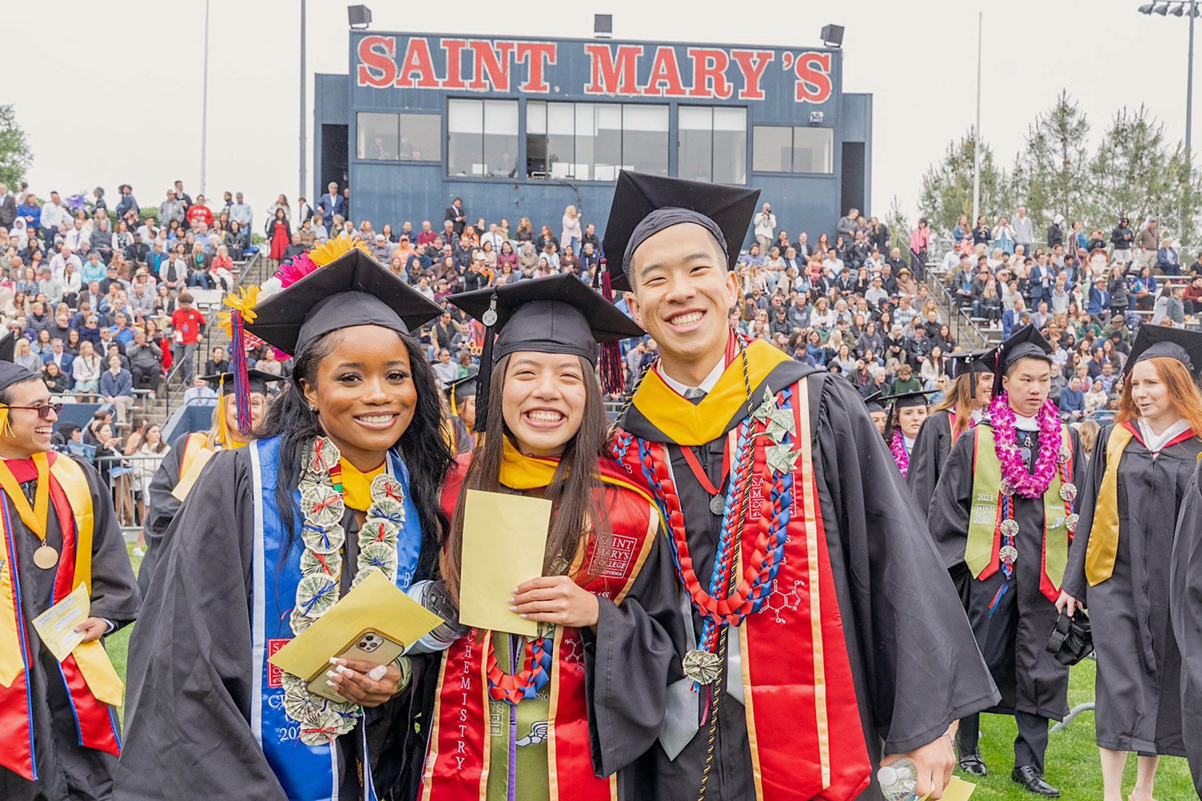 At 2023 Commencement, three students beneath the Saint Mary's sign on the soccer field