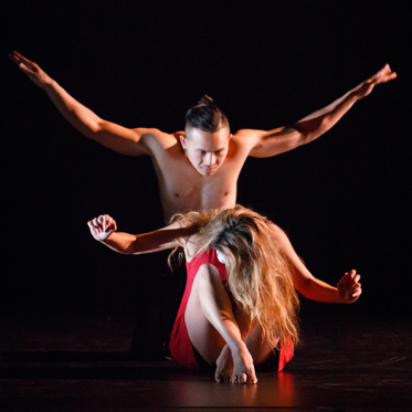 Shirtless male dancer arms wide over female dancer in red dress