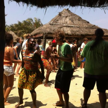 people standing outside in the sun under a hut