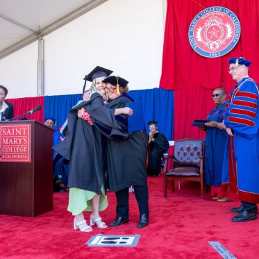 A graduate hugging an administrator on stage