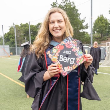 A graduate holding a cap that says Miss Berg