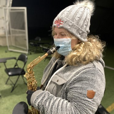 A musician dressed in grey winter clothing playing their saxophone outside