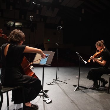 Two musicians, both playing string instruments, performing on stage in LeFevre theatre
