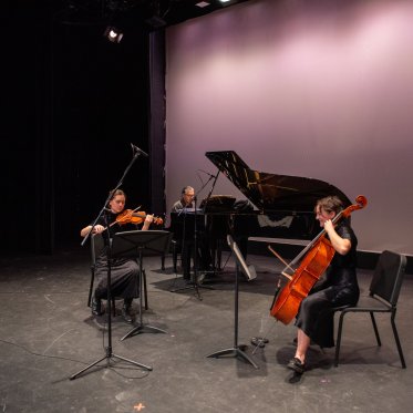 Two musicians, both playing string instruments, perform on stage in LeFevre theatre accompanied by a pianist