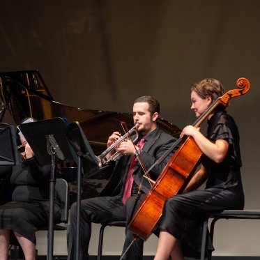 A trumpet player and Desiree Sturrock playing her cello perform on stage at 