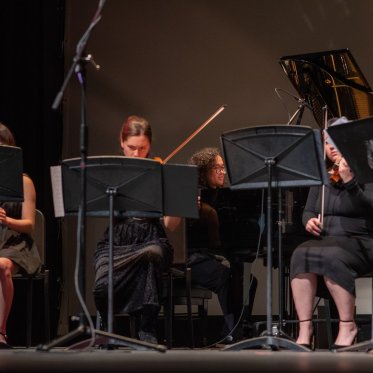 A row of musicians, dressed in black, performing on stage at LeFevre Theatre