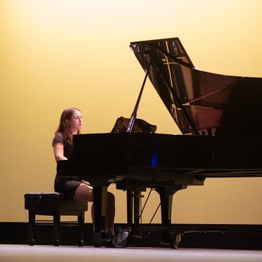 A female piano player performing on stage against a soft yellow backdrop at LeFevre Theatre