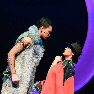 A still from "A Midsummer Night's Dream" with Puck being threatened by another character. Behind them, a crescent moon. 