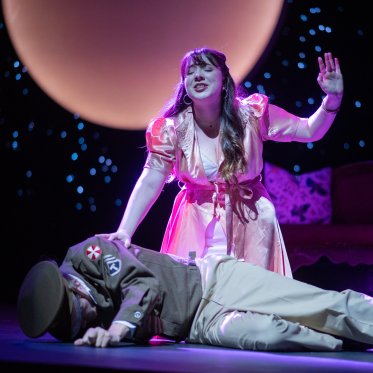 Send It To The Moon -- A woman donning a pink dress mourns over the body of a man wearing a WWI military-officer outfit. One of her hands is on the fallen man's shoulder, the other raised.  Behind them, a pink moon against a cosmic backdrop.