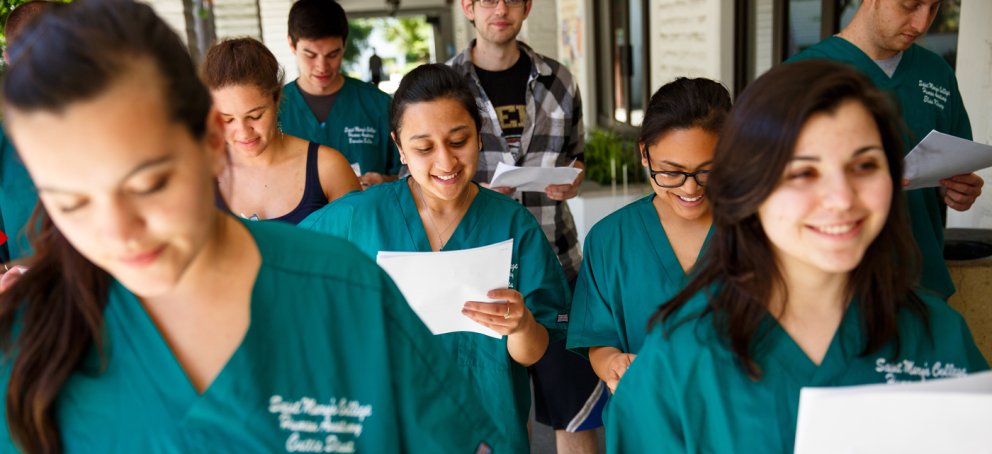 Students looking at papers while wearing scrubs and walking down the hall