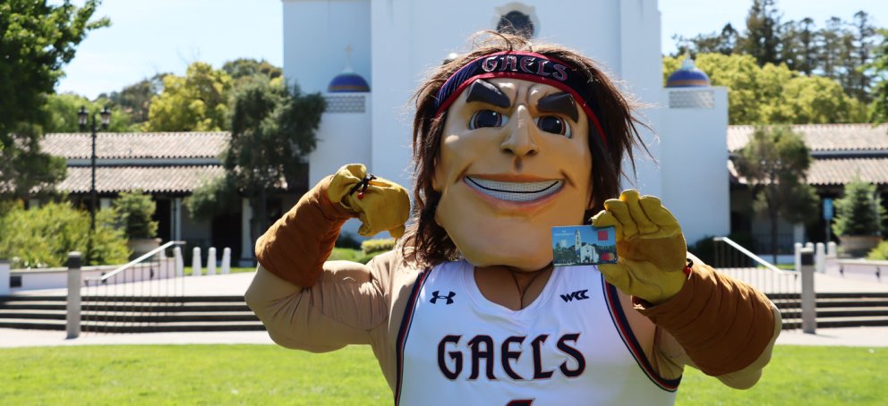 Gideon the mascot holding a credit card in front of the Saint Mary's College Chapel
