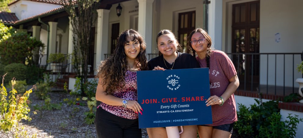Three students hold a One Day One SMC sign at Saint Mary's campus