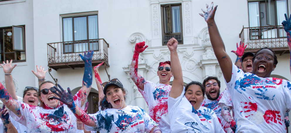 A diverse group of people smiling, each with colorful paint on their faces, celebrating together in a lively atmosphere.