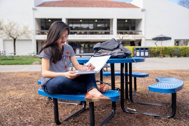 A student studying on a bench in the middle of SMC's campus