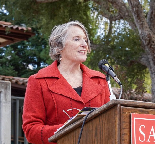 Professor Rosemary Graham in Red jacket speaking at podium outdoors