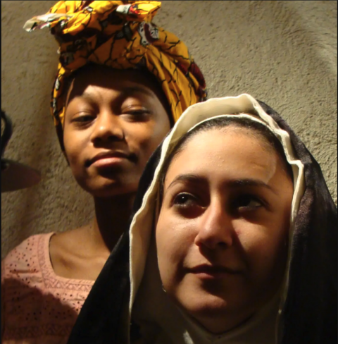 A close-up shot of a nun next to a girl with a headwrap looking at her, smiling.