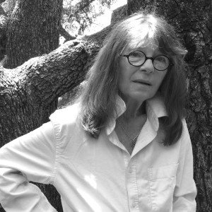 black and white photo of poet dorianne laux in a white shirt in front of a background of trees