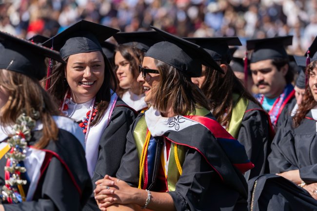 Friends in grad robes seated in a scene from Commencement 2025