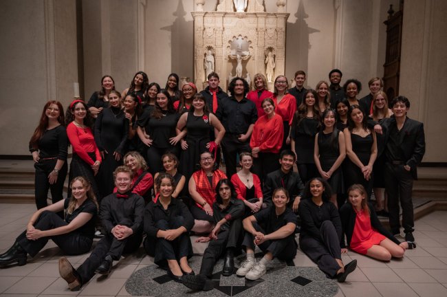SMC Choir Fall '25 with students standing and sitting in front of the altar dressed in black with red accents.