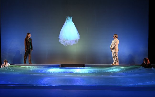 a glowing, floating wedding dress between two actors on the stage