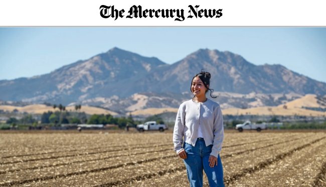 Individual standing in field and smiling with mountains behind