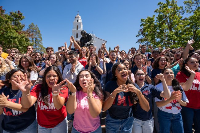 Dozens of students smiling and cheering at the camera in front of the Chapel