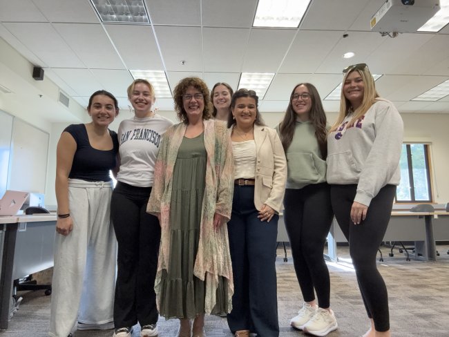 Group of eight people, seven female students and one female professor standing in a classroom for Italian