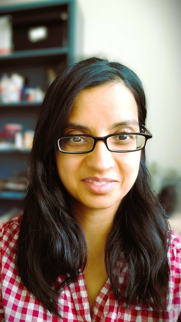 Image of woman with black hair, brown skin and glasses showing head and shoulders