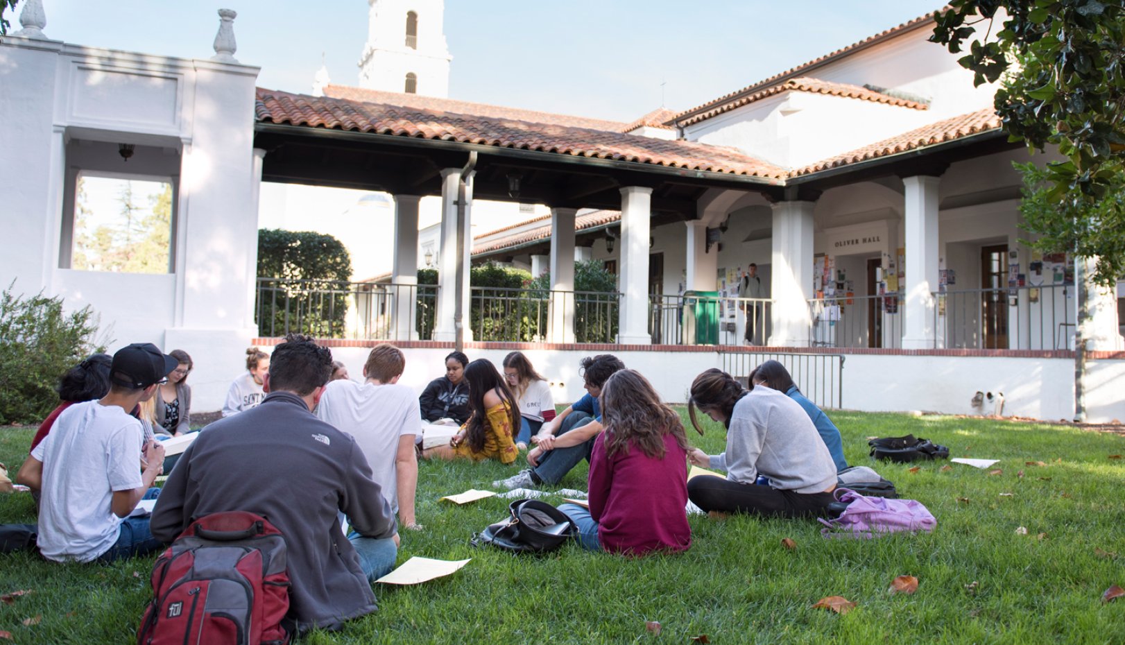 A class sitting outside in a circle with the SMC chapel in the background