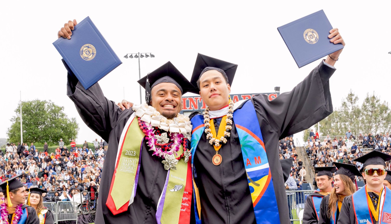 Two students raising their diplomas at 2023 Undergraduate Commencement