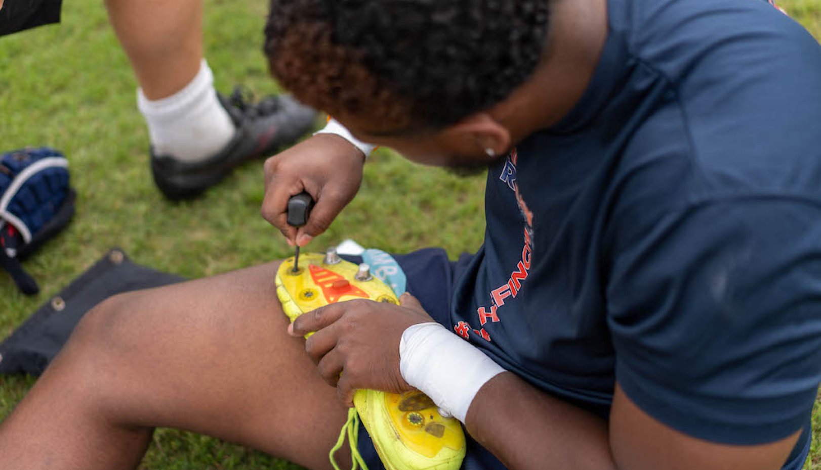 A Gaels' men's rugby player adjusts his cleats before 2024 National Championships