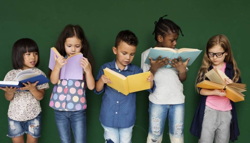 Five children standing next to each other, all reading books