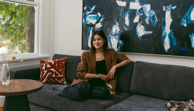 Sierra Nguyen sits on a sofa with a large, blue painting behind her