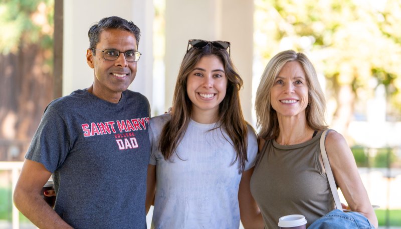 A student and her parents smile for a photo during Family Weekend
