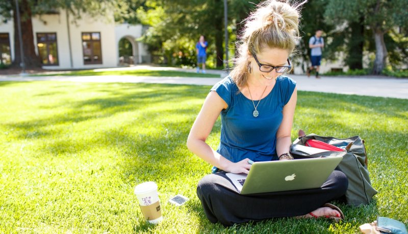 Student working on laptop while sitting on the lawn
