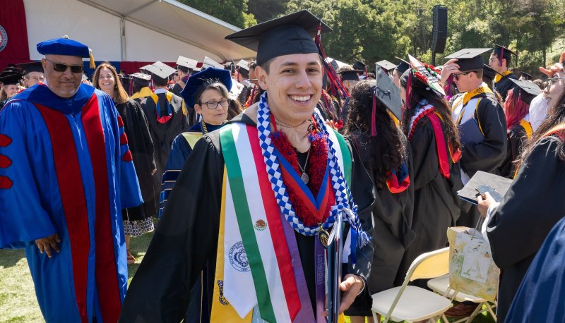 Isaac, in graduation cap and gown, smiles at the camera amongs dozens of his classmates