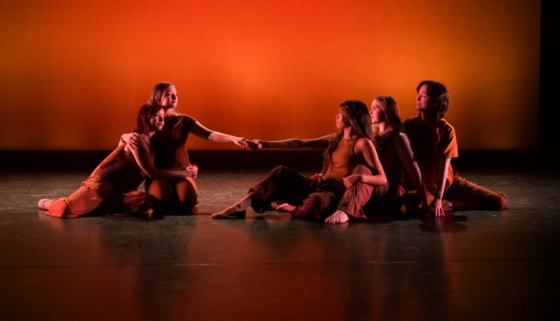 Modern dancers sitting on the stage floor in costume with an orange hue in the background