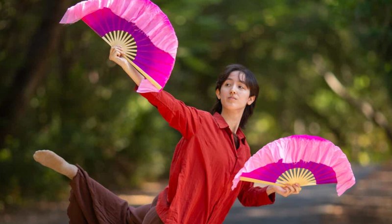 Anya Tang in a dance pose outdoors with Japanese fans in his hands