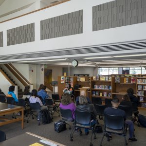 A group of students, faculty, and staff gathered on the second floor of the library listening to a poetry reading.