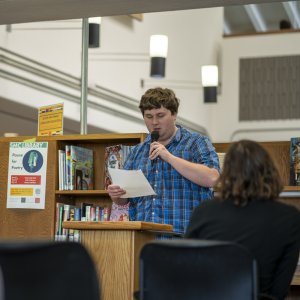 A student wearing a blue shirt reading at Pause for Poetry.