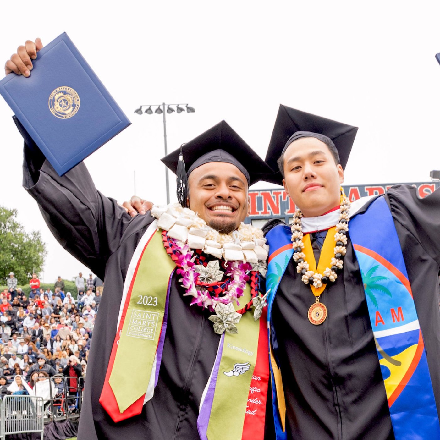 Two students raising their diplomas at 2023 Undergraduate Commencement