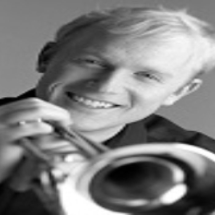 A black-and-white headshot of Scott Macomber holding a trumpet