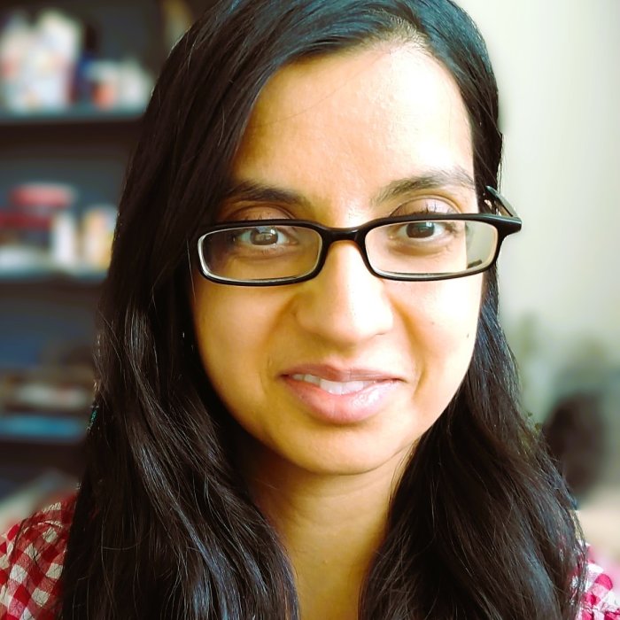 Image of woman with black hair, brown skin and glasses showing head and shoulders