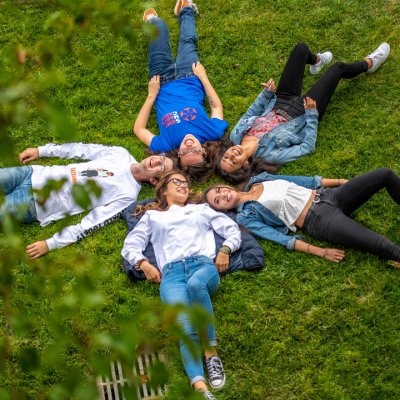Students laying on the grass with their heads together in a star shape