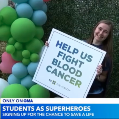 A female Saint Mary's student holds a sign that says "Help Us Fight Blood Cancer"