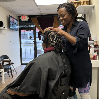 A woman sits in a salon chair while a hair stylist works on her hair.
